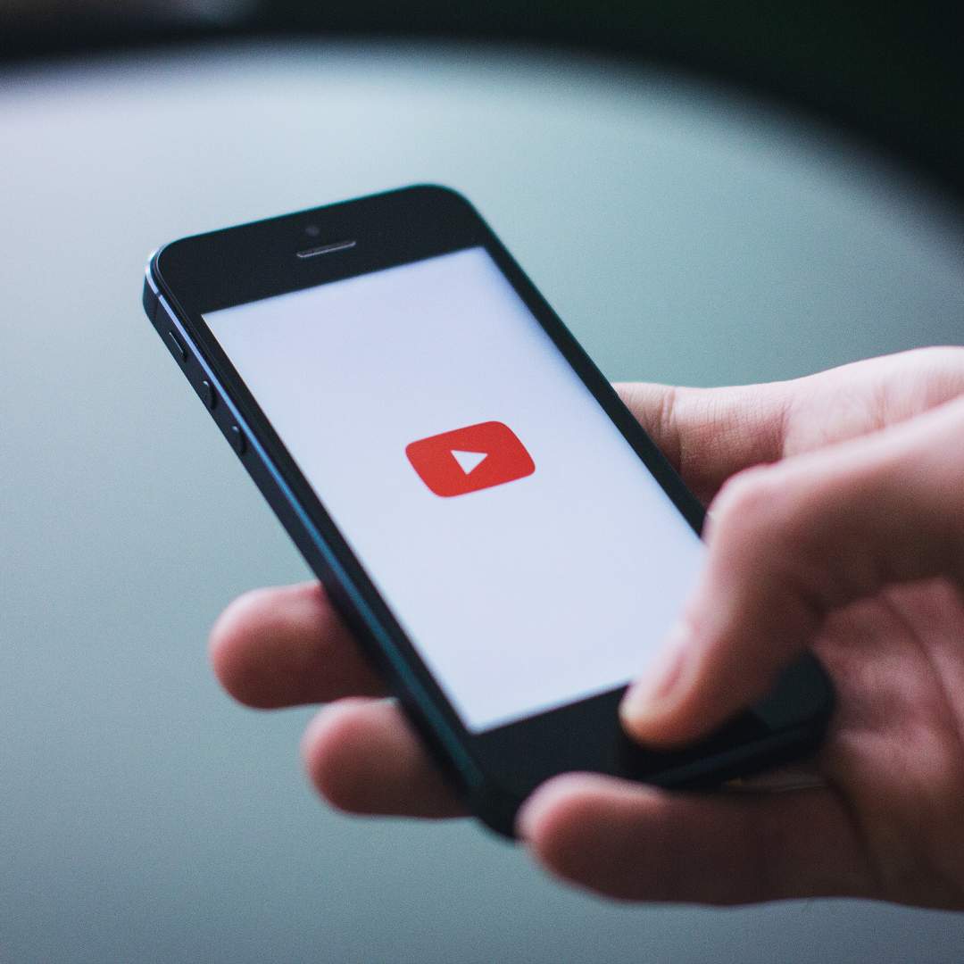 Imagem de uma pessoa segurando o celular com o logo do YouTube